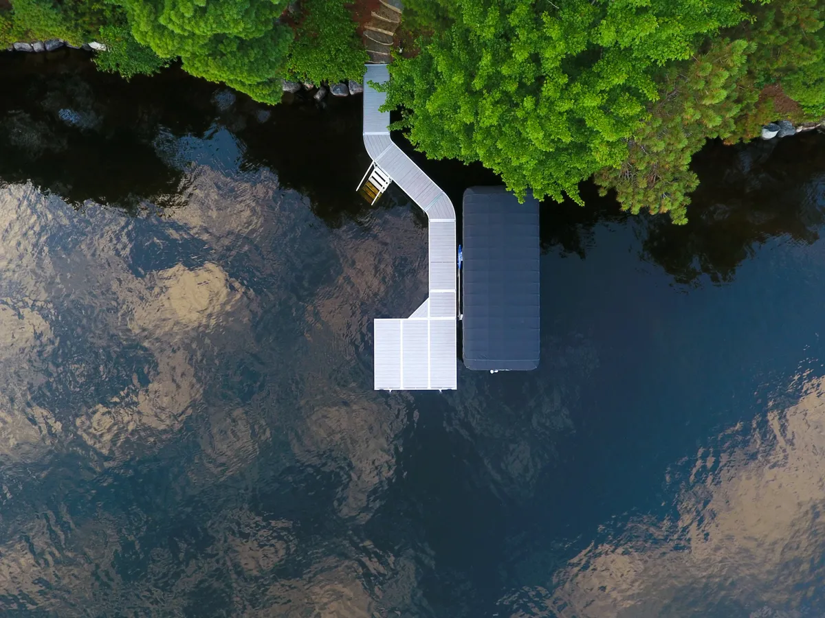 An aerial view of a modular floating dock system extending from a tree-lined shore into the water. 