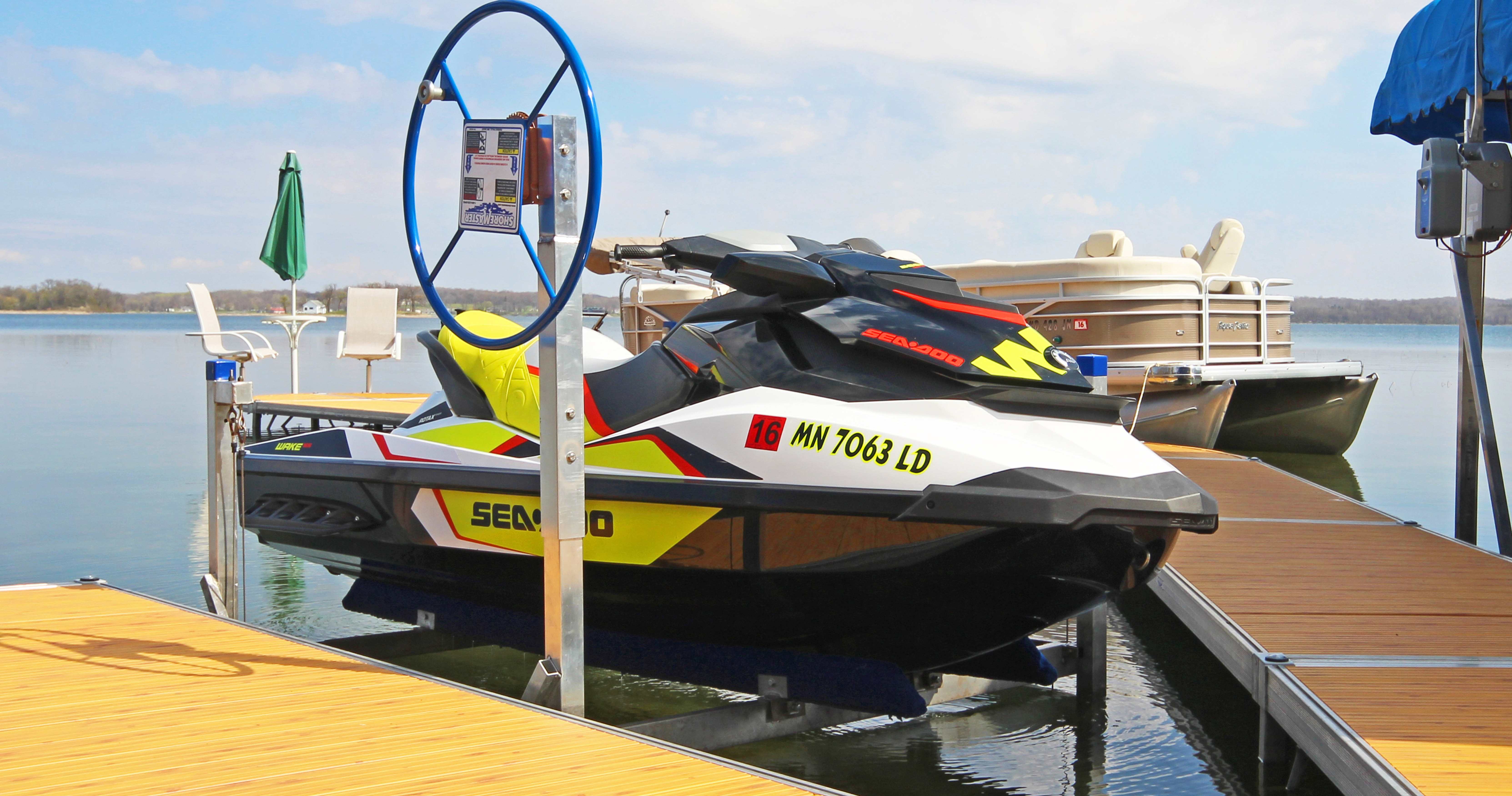 Sea-Doo jet ski parked on a dock lift beside a lake with a pontoon boat in the background.