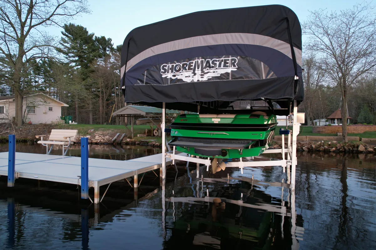 A bright green speedboat resting on a white boat lift with a black ShoreMaster canopy next to a dock.
